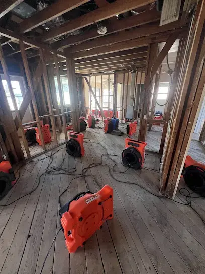 Air movers set across the subfloor of a house opened down to the framing for drying.