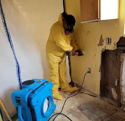 Technician in a protective suit cutting out wet drywall beside an air mover during a Granada Hills dry-out