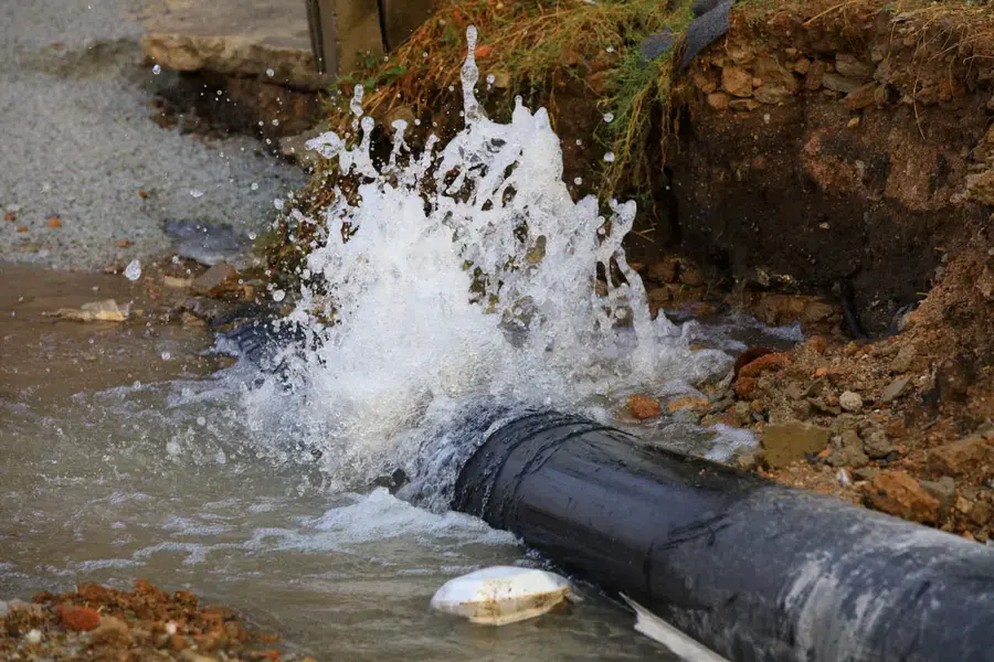 Water bursting from a broken underground pipe in an open trench