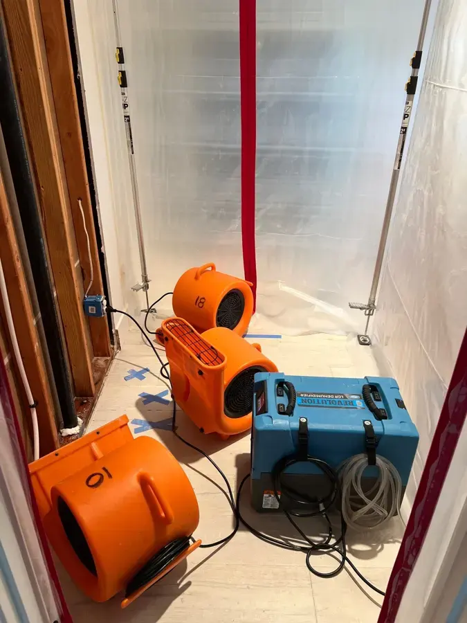Air movers and a dehumidifier running inside plastic containment in a hallway during a Burbank water damage job